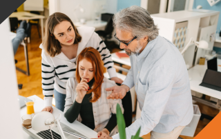 2 women and one man gathered around a desk discussing how to harness the power of delegation for high-performing teams.