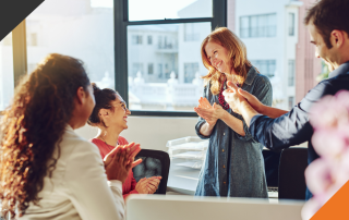 three employees gathered around a fourth employee experiencing the power of employee recognition