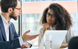 a male coworker is speaking with a female coworker at a desk focusing on how to stop micromanaging a team